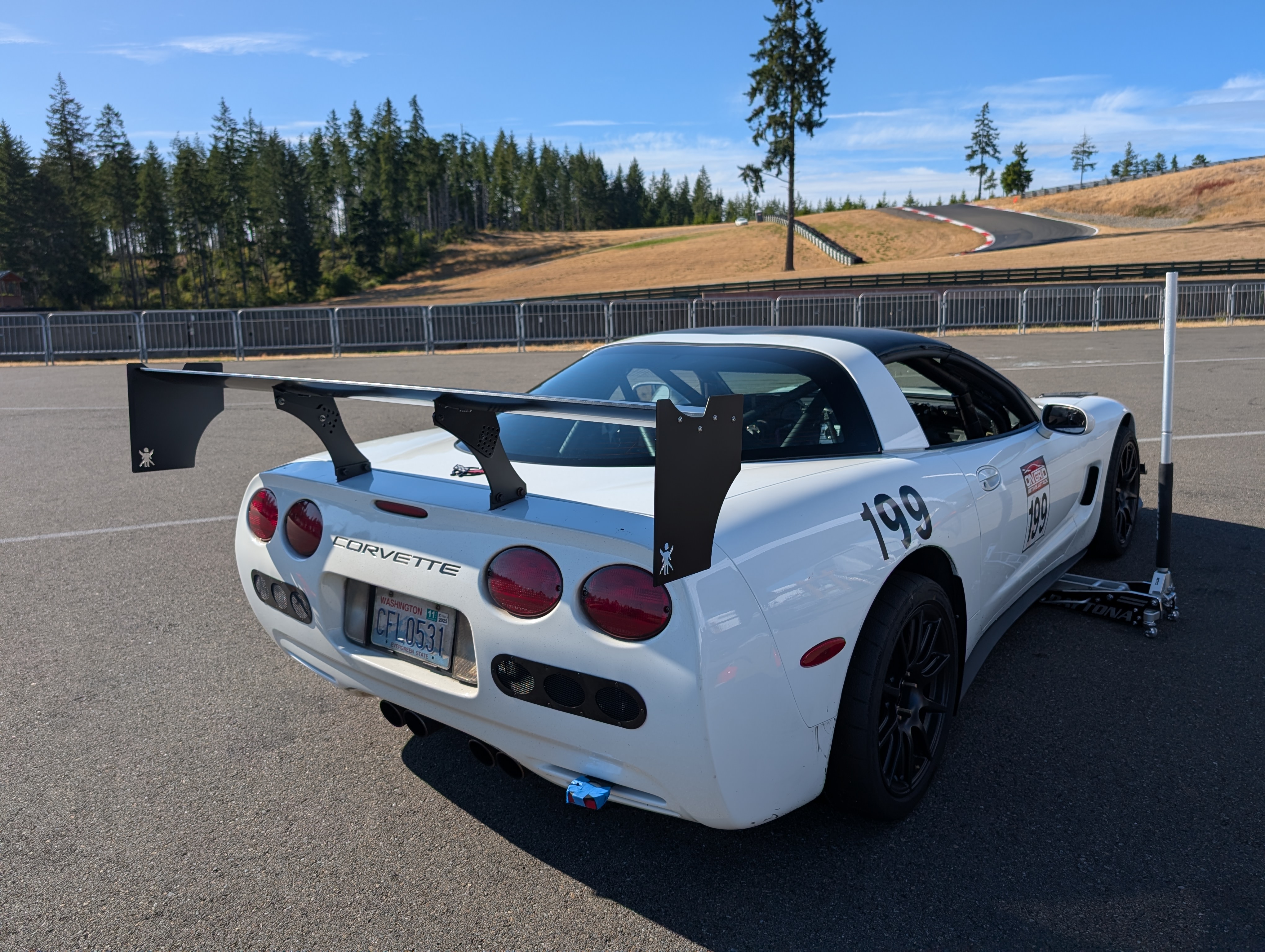 Rear view of the #199 1999 C5 Corvette at the Ridge Motorsports park. In the background are the final turns before the straight. The car has a 9 Lives Racing Wing prominently mounted on the rear of the car.