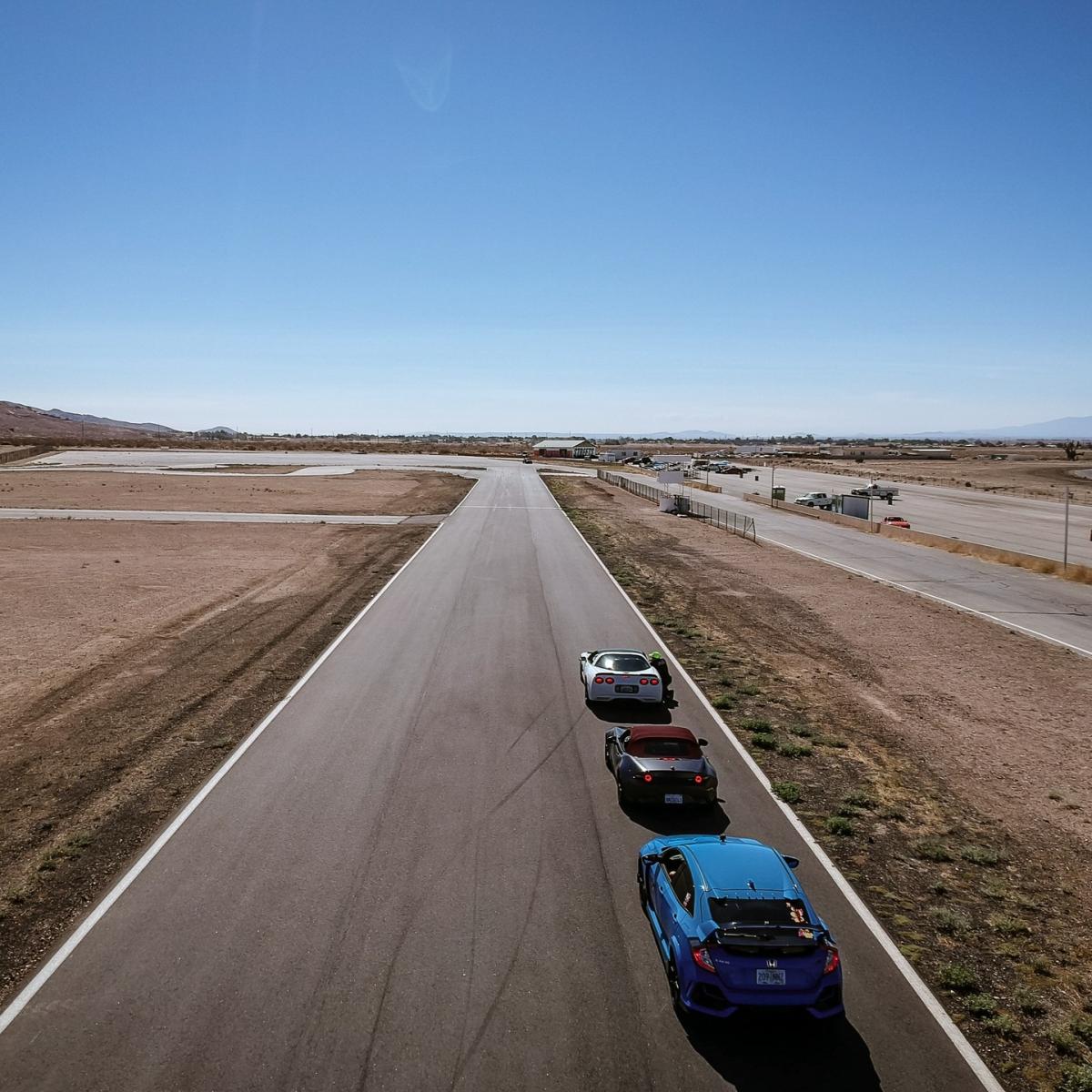 A C5 Corvette wis at the front of a line of cars on track. They are lined up to do a training drill.