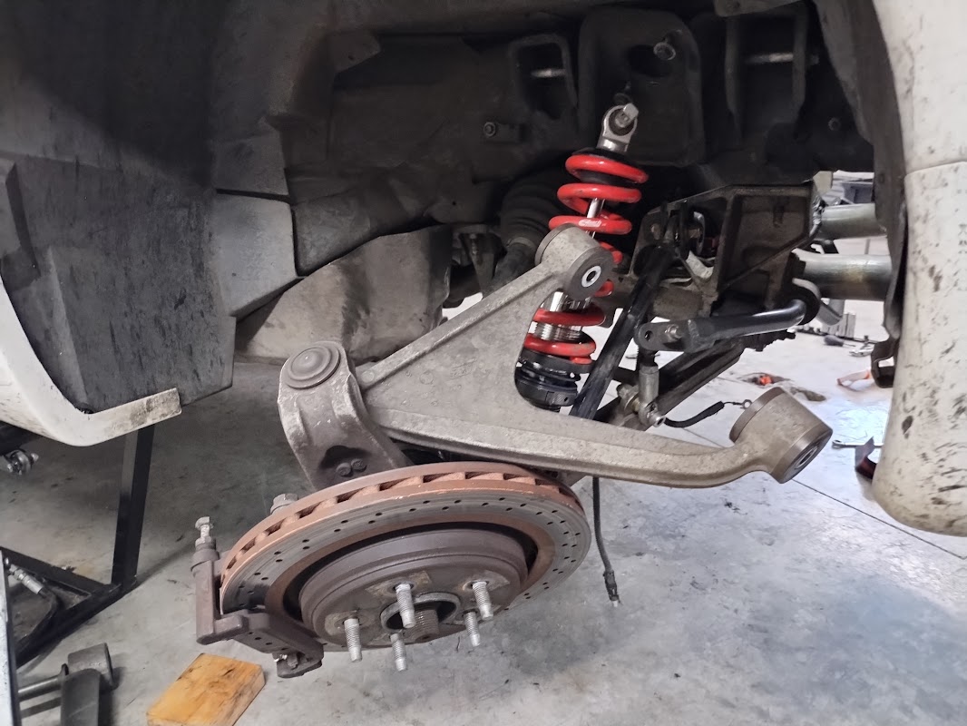 The rear drivers side wheel well of a C5 Corvette, with the upper control arm disconnected and the kunckle just hanging loose, held on only by the lowers and the coilovers.