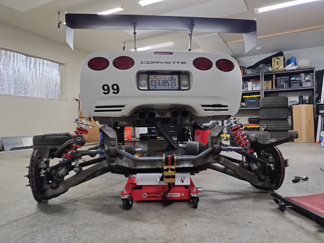 Rear of a white C5 Corvette with wing that has it's rear subframe dropped and sitting behind the car