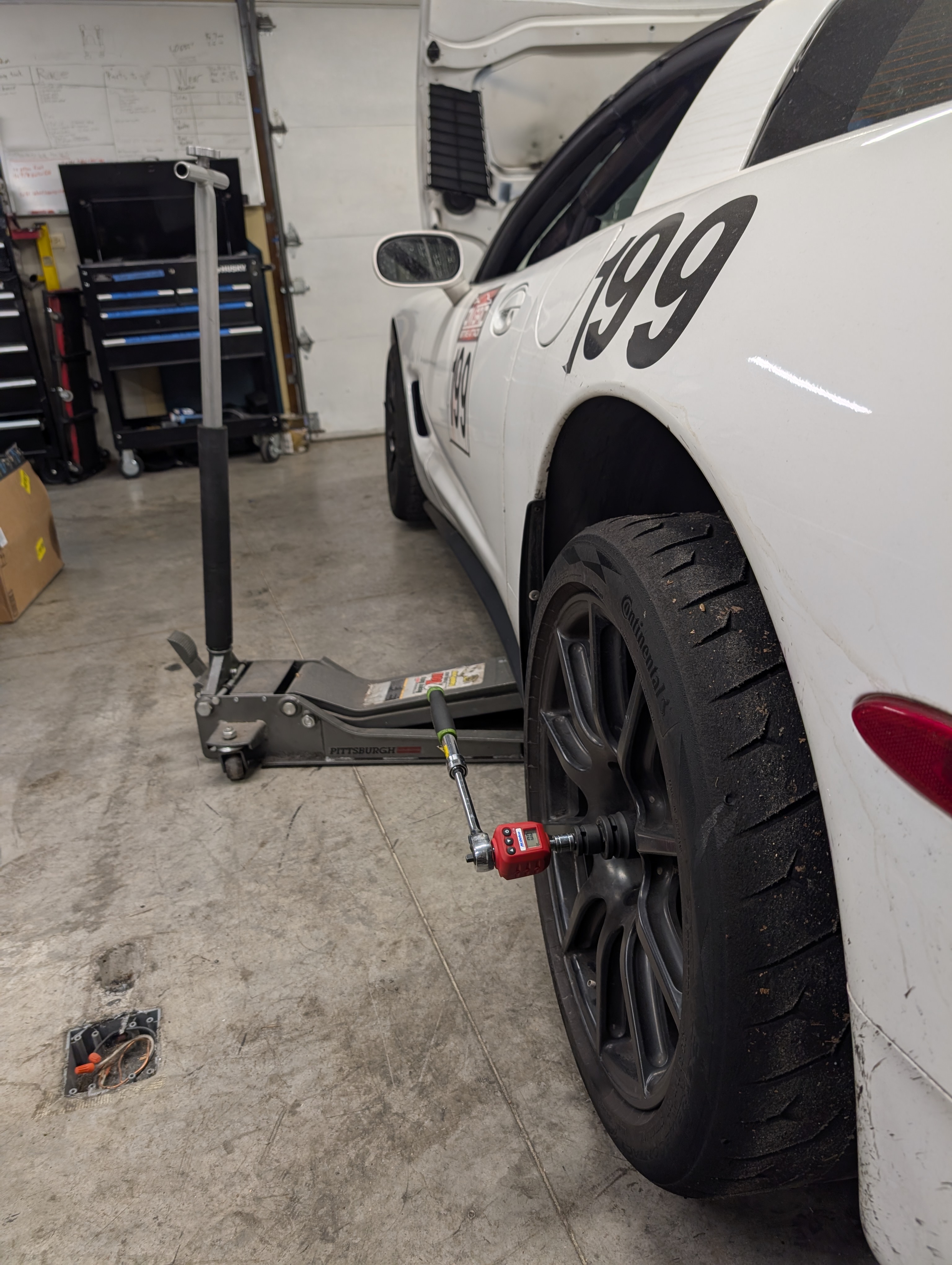 A side shot of a C5 Corvette, where one side is jacked up and a ratchet with digital torque adapter is on the lift rear axle nut to allow for measuring torque.