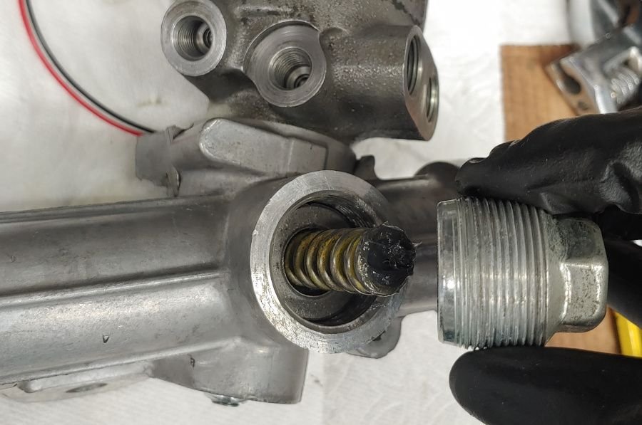 A picture of the C5 Corvette steering rack tension adjuster with the adjuster removed, showing a large spring under it.