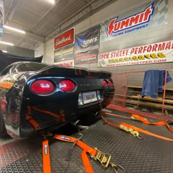 A c5 Corvette on the dyno, pictured from the rear with multiple tie downs keeping the car in place.
