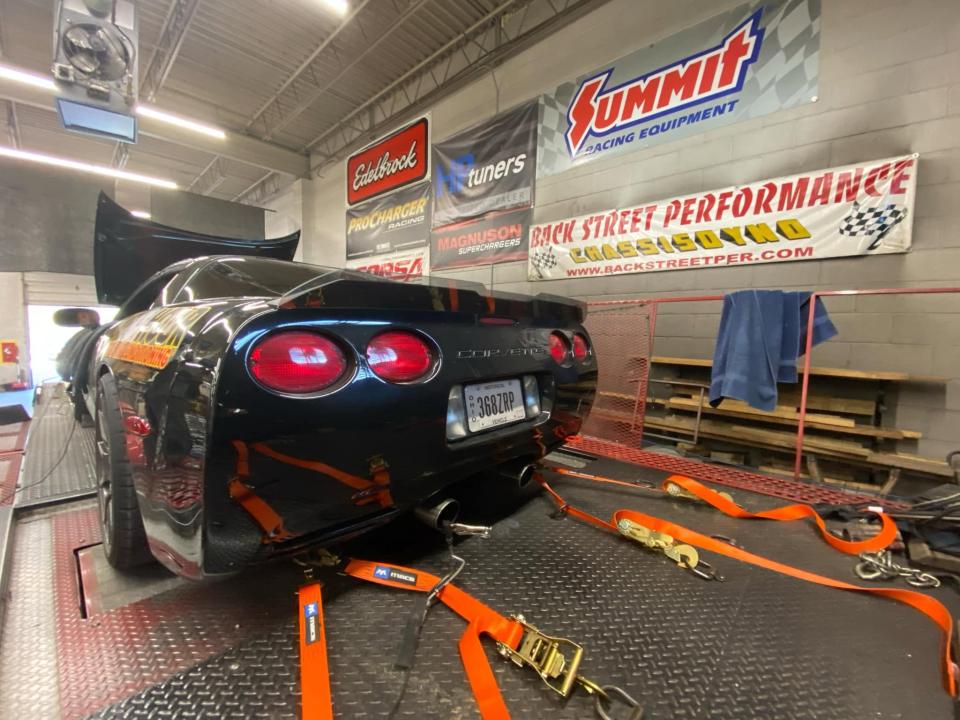 A c5 Corvette on the dyno, pictured from the rear with multiple tie downs keeping the car in place.